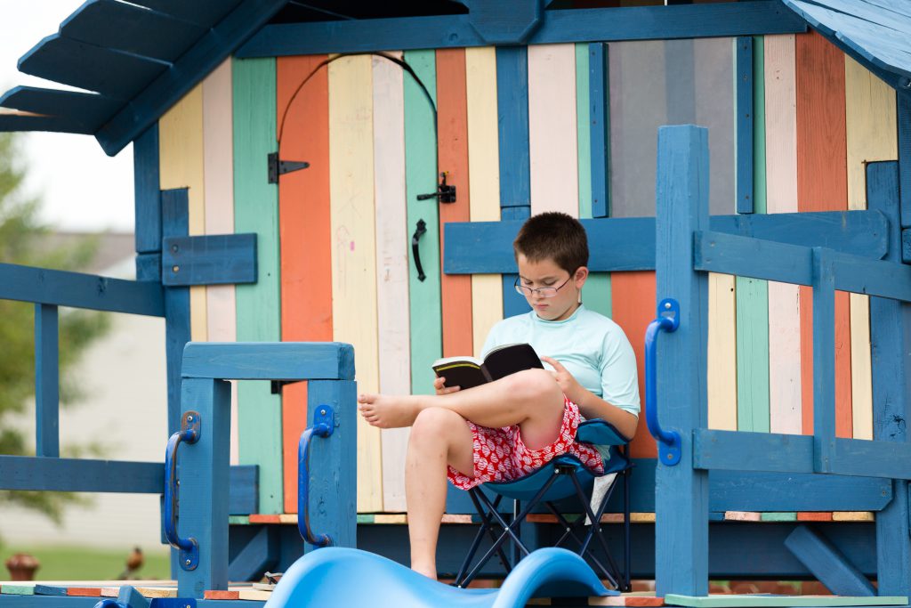 Young boy sitting reading on a wooden playground