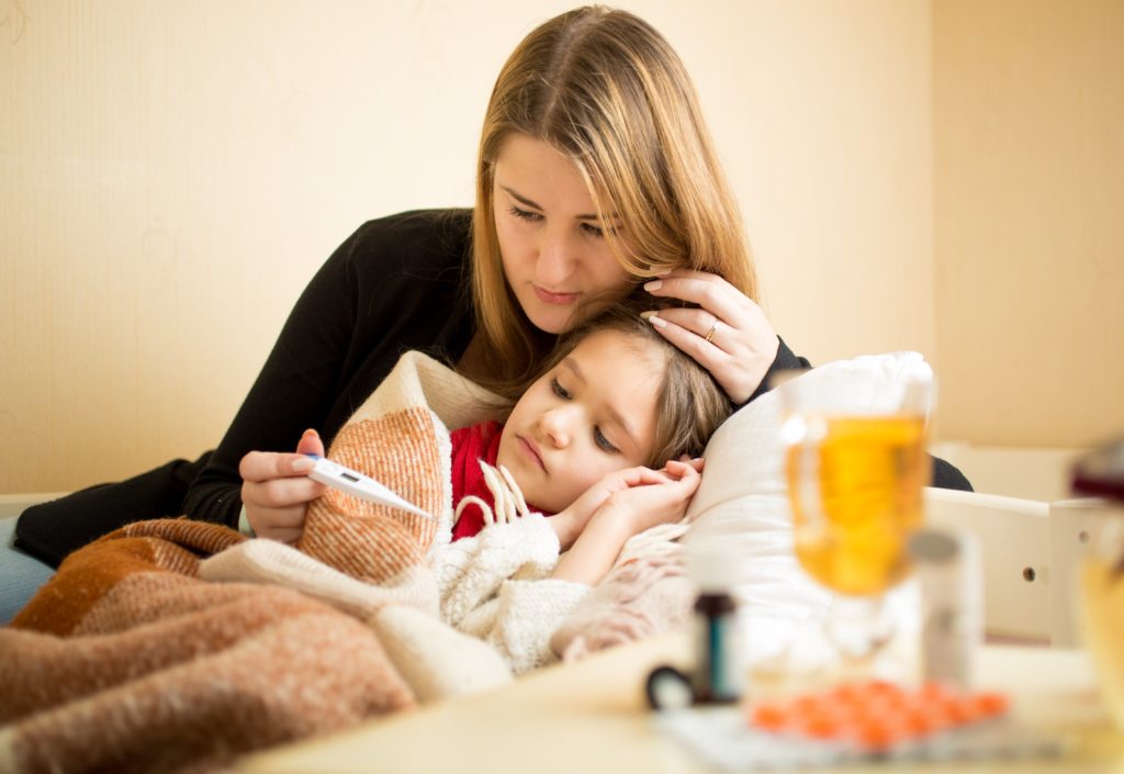 Mother taking temperature of sick daughter in bed