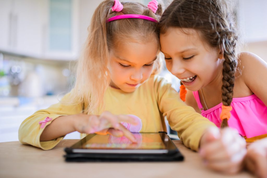 Two young girls playing with iPad on table