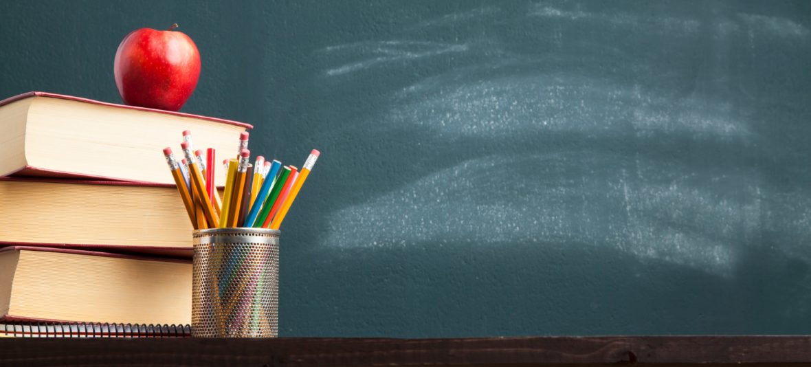 A chalkboard and a desk with an apple and pens on it.