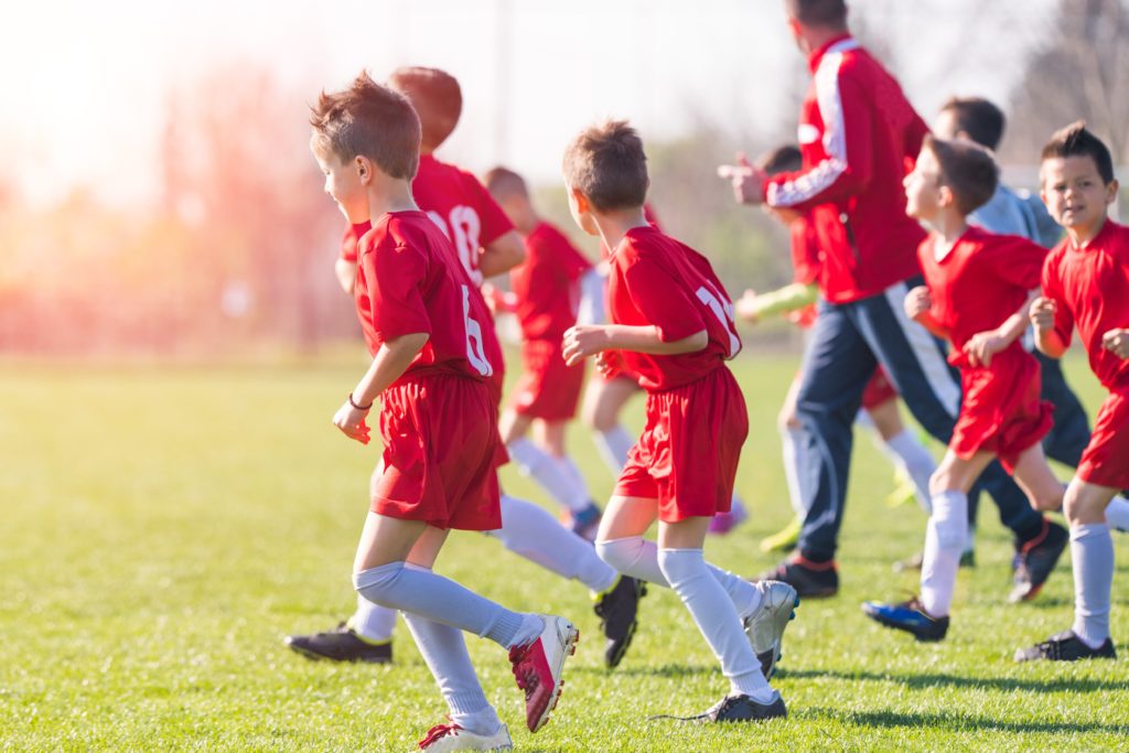 Young soccer players run onto the field with their coach. 