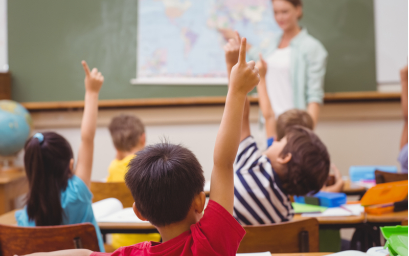 Young pupils raising their hand in class to answer a question