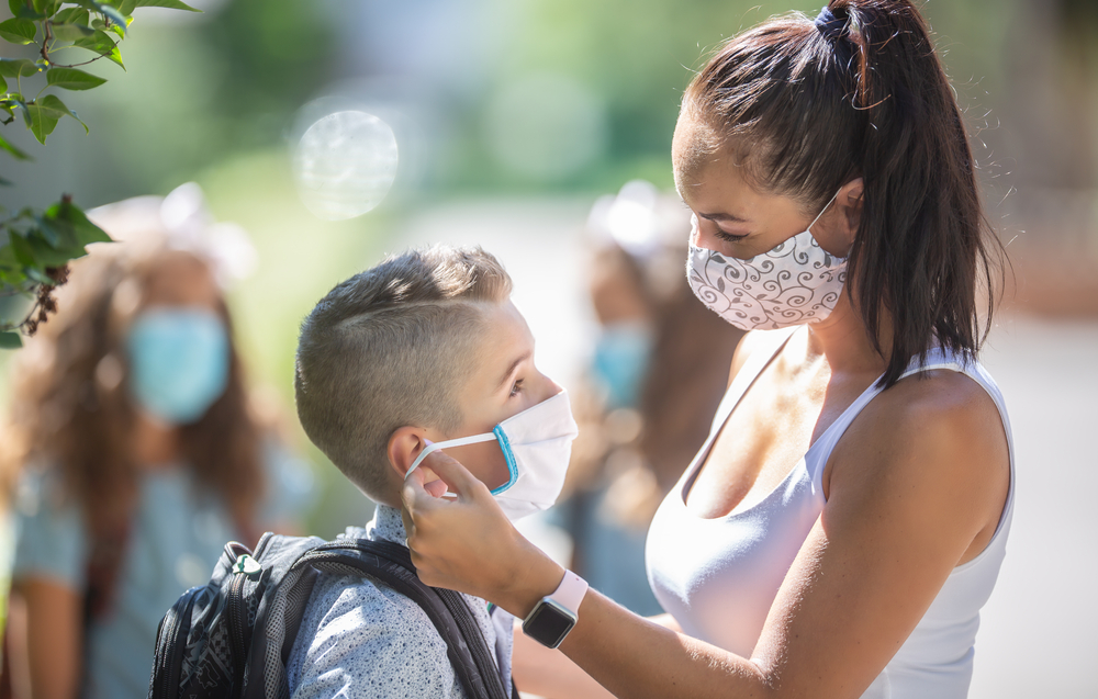 Masked boy with mother getting ready for school