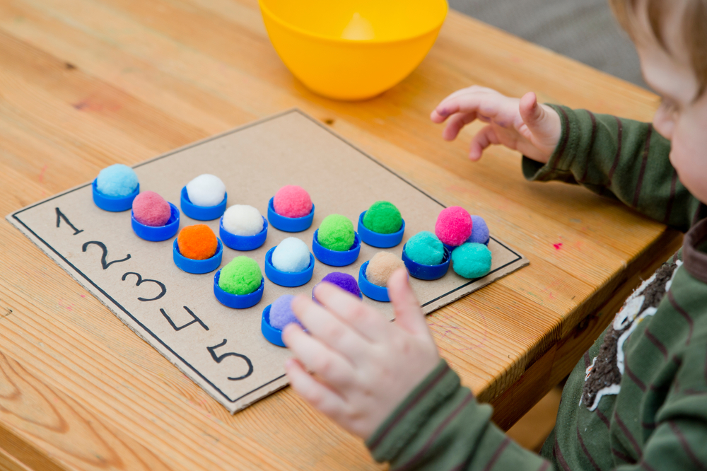 Boy learning math with colored pom poms