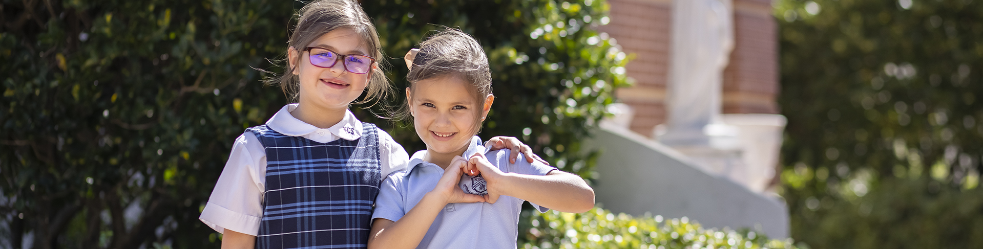 two young female girls in blue checked uniforms with white shirts smiling at the camera