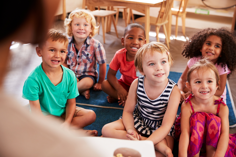 pre-k students sitting on the floor listening to teach read a story