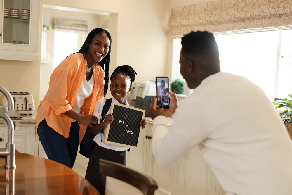 Smiling parents with child and first day of school sign after transferring to St. Cecelia